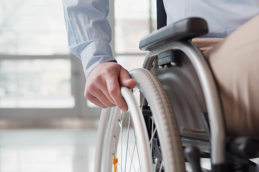 Close up of disabled man riding in wheelchair. Cropped shot of handicapped male holding hand on wheel of wheelchair indoors. Office worker in wheelchair in business center