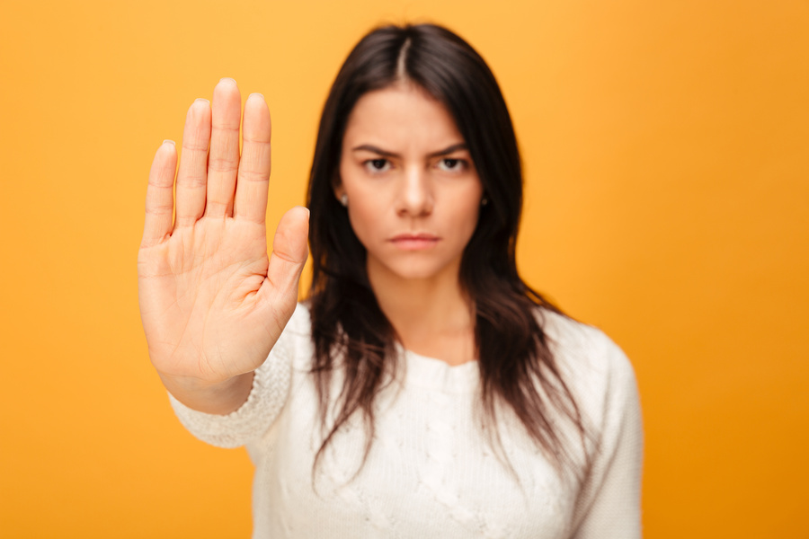 Portrait of a serious young woman showing stop gesture with her palm isolated over yellow background